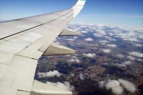 Asa de avião no ar, com visão de cidade abaixo das nuvens