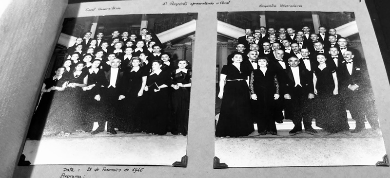 Detalhe de um álbum de fotos antigas, em preto de branco, presas com cantoneiras. As fotos mostram um grupo de músicos em trajes de gala, ladeando o regente Leon Kaniefsky
