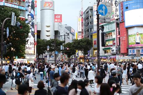Multidão caminha em rua em Tóquio, com muitas placas e anúncios coloridos, durante o dia