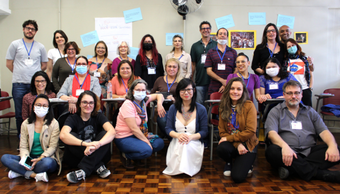 Foto de grupo de funcionárias e funcionários da ECA posando; à frente, as funcionárias estão sentadas; atrás delas outras funcionárias estão sentadas em carteiras escolares; ao fundo, em pé, os demais funcionários e funcionárias, além dos dois ministrantes do curso.