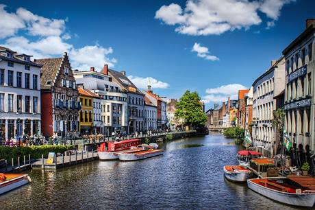Barcos pequenos ao longo de rio com casas coloridas típicas dos dois lados das margens, em Gante,na Bélgica