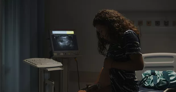 Em cama de hospital, mulher grávida coloca a mão sobre a barriga