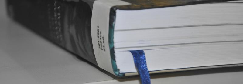 Close do corte e parte da lombada de um livro, mostrando etiqueta com número da biblioteca e fita azul marca-páginas