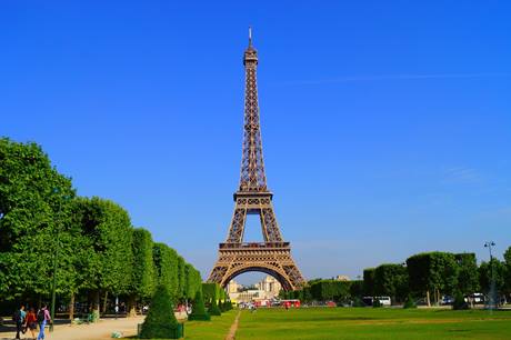 Dia ensolarado sem nuvens, em campo rodeado por árvores que segue até a Torre Eiffel