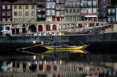 Barco pequeno amarelo na margem de rio com pedras em Porto, Portugal, construções ao fundo
