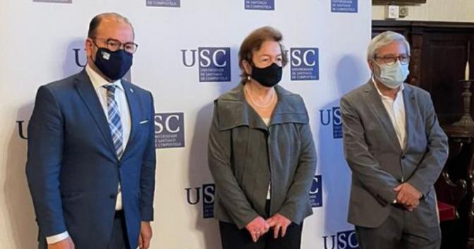 Margarida Kunsch, ao centro, e dois representantes da USC. Na imagem, os três posam para foto, usando máscaras e mantendo distanciamento um do outro. Ao fundo, banner com a sigla USC.