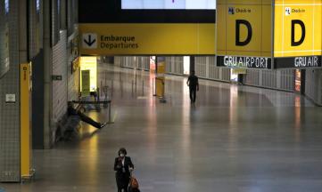 corredor da área interna do aeroporto de guarulhos, com poucas pessoas, usando máscaras. No canto superior da imagem, uma placa amarela indica a área de embarque