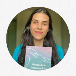 Foto de Camila com seu livro em mãos. Ela é uma mulher de pele branca um pouco bronzeada, olhos escuros e cabelos grandes, escuros e levemente ondulados. Sua roupa é azul. Ela sorri para a câmera segurando um exemplar do livro. A capa do livro é rosa e verde, com o desenho das mãos de uma mulher e um bebê e o título da obra em branco.