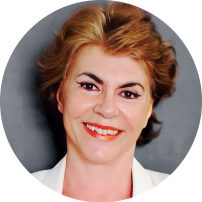 Foto de uma mulher branca sorrindo. Ela tem cabelos avermelhados, lisos e curtos, olhos castanhos, veste blusa branca e usa batom vermelho.  Atrás dela, um fundo cinza.