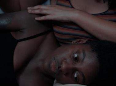 Uma mulher negra, usando camisa preta, deitada no colo de outra mulher, olhando para baixo. 