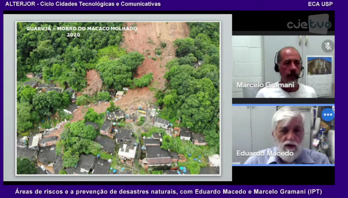 Captura de tela da transmissão Áreas de riscos e a prevenção de desastres naturais. Na imagem, do lado esquerdo da tela e em maior proporção, há uma uma fotografia do Morro do Macaco Molhado, no Guarujá, em 2020. A foto conta com a visão aérea de casas localizadas abaixo do morro, rodeadas de árvores e afetadas por um deslizamento de terra. Do lado direito, em menor proporção, a imagem de dois homens brancos que falam.