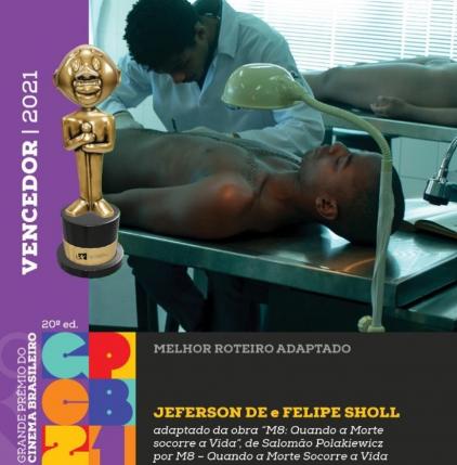 Arte oficial da 20ª edição do Grande Prêmio do Cinema Brasileiro mostra fotografia de uma cena do filme M8 - Quando a Morte Socorre a Vida. Um médico legista negro, de cabelos pretos crespos e curtos, usando jaleco e luvas brancas, realiza uma autópsia no corpo de um jovem negro de cabelos raspados. Na parte inferior da imagem aparecem o logo do Prêmio e os dizeres em letras brancas e amarelas sobre um retângulo preto: Melhor Roteiro Adaptado: Jefferson De e Felipe Sholl, adaptado da obra M8 - Quando a Morte Socorre a Vida, de Salomão Polakiewicz por M8 - Quando a Morte Socorre a Vida. Na parte esquerda da imagem, sobre um retângulo roxo em letras brancas, aparecem os dizeres Vencedor 2021 ao lado de uma reprodução do Troféu Grande Otelo.