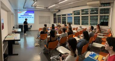 Foto colorida em ambiente interno, de uma sala de reunião com estudantes estrangeiros e a secretária da CRInt, Thaise Desirre, os recepcionando