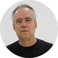Foto de homem branco, calvo, com cabelos curtos, lisos e grisalhos. Ele veste uma camiseta preta. O fundo é branco.