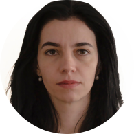 Foto  de mulher branca com cabelos castanhos escuros e lisos e olhos castanhos. Ela usa brincos de pérola. O fundo é branco.