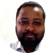 Foto de homem negro com olhos castanhos, cabelos  e barba escuros e curtos. Ele veste camisa branca. O fundo é branco.