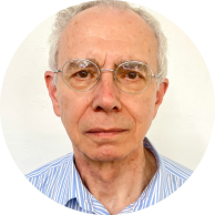 Foto de homem branco com cabelos, curtos, lisos e grisalhos. Ele usa óculos de armação fina e arredondada e veste uma camisa azul listrada. O fundo é claro.
