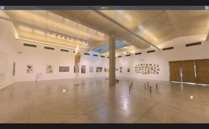 A imagem reproduz um espaço expositivo amplo, retangular, com uma coluna localizada à esquerda da foto. O chão é cinza. Nas paredes, brancas, estão penduradas, nove obras de arte, uma ao lado da outra. No chão, uma obra de arte é composta por placas retangulares na cor bege, algumas empilhadas e outras caídas umas próximas das outras. O teto e acinzentado, com trilhos de iluminação