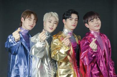 Quatro rapazes de origem asiática chamam o leitor com a mão. Todos usam trajes coloridos (azul, branco, amarelo e rosa) e um (ao centro) possui cabelo totalmente descolorido.