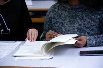 Foto colorida em ambiente interno, de dois estudantes lendo livros lado a lado