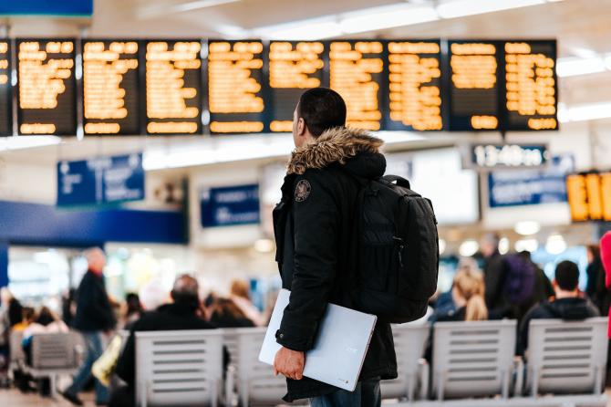 Jovem observa painel de voos em saguão de aeroporto