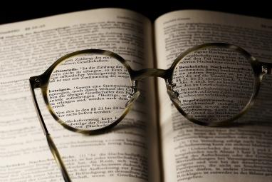 Foto colorida, em ambiente interno, de óculos de grau repousando sobre livro aberto