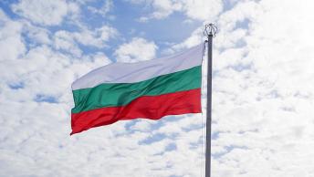 Foto colorida em ambiente externo, da bandeira da Bulgária, e ao fundo o céu azul