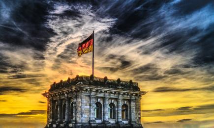 Foto colorida em ambiente externo, de um entardecer com a bandeira alemã esvoaçante em foco principal