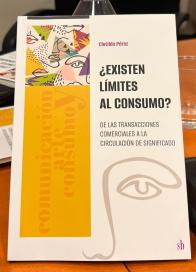 Fotografia da capa de um livro que está sobre uma mesa. O fundo é branco  e tem do lado direito o nome da autora, Clotilde Perez, o título e subtítulo, “?Existen límites al consumo? De las transacciones comerciales a la circulación de significado” e a ilustração  de um olho e um nariz. À esquerda, há uma ilustração com olhos, bocas e narizes e uma faixa amarela com os escritos na vertical, “comunicación arte y consumo” 