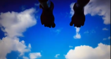 Foto do céu azul com nuvens. Na parte superior, tem-se a silhueta de dois pés com os dedos para baixo.