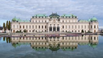Palácio Belvedere, em Viena, na Áustria, com telhados verdes, paredes claras e inúmeras janelas, construído em frente à um espelho d'água