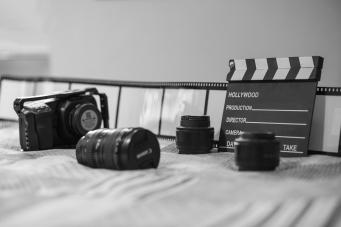 Câmera, lentes e claquete em cima de tecido cinza
