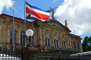 Bandeira da Costa Rica hasteada em frente ao Teatro Nacional do país, sob céu com nuvens