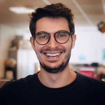 Foto de Diogo Cortiz, um homem branco, de cabelos curtos e castanhos. Usa óculos redondos de aro preto. Tem cavanhaque e bigode castanhos. Ele sorri olhando para a câmera.