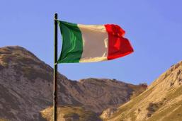Bandeira italiana hasteada em frente à montanhas sem vegetação, sob céu azul