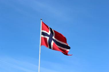 Foto colorida, em ambiente externo, da bandeira da Noruega hasteada sob céu azul