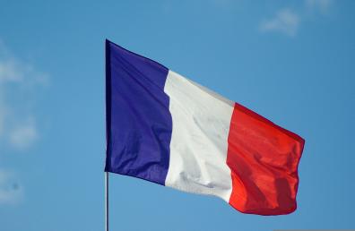Foto colorida em ambiente externo, da bandeira da França ao vento com o céu azul de fundo