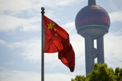 Foto colorida, em ambiente externo, de bandeira da China hasteada ao lado da Torre Pérola Oriental, em Xangai