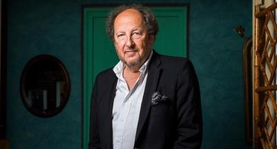 François Jost é um homem branco, parcialmente calvo, barba rala, na faixa dos 70 anos; veste uma camisa branca e um paleto azul marinho; ao fundo uma porta verde e uma parede azulada.