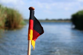 Pequena bandeira da Alemanha em frente à corpo d'água desfocado, rodeado por capim