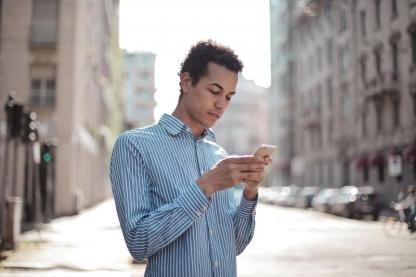 Foto de homem vestindo uma camisa azul mexendo no celular na rua.