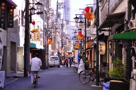 Foto colorida, em ambiente externo, de rua estreita no Japão, com placas de estabelecimentos e decorações vermelhas nos postes.