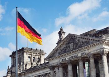 Foto colorida em ambiente externo, da bandeira da Alemanha em frente ao Palácio do Reichstag 