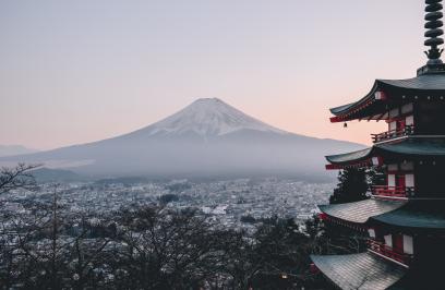 Foto colorida em ambiente externo, de um prédio tradicional japonês e, ao fundo, uma cidade japonesa e o Monte Fuji