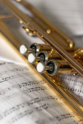 Foto de detalhe de um trompete dourado sobre uma partitura de música.