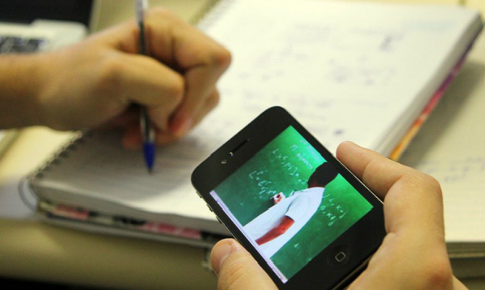 Foto de uma pessoa branca segurando um celular e fazendo anotações à caneta em um caderno. A imagem não mostra outra parte do corpo além das mãos.