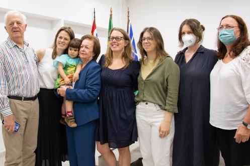 Foto de oito pessoas, um homem, uma criança e sete mulheres. Os adultos estão em pé e a criança está no colo. Todos são brancos e a maioria das mulheres têm cabelos lisos e claros. O homem é um senhor de cabelos grisalhos.