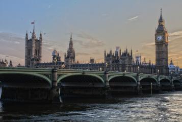Foto colorida em ambiente externo, de Londres, com uma paisagem da torre Big Ben e do Rio Tâmisa ao entardecer.