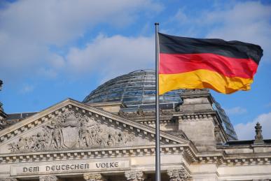 Foto colorida em ambiente externo, da bandeira da Alemanha na frente do prédio do Parlamento de Berlim