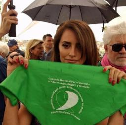 Foto colorida mostra Penélope Cruz, uma mulher de pele bronzeada e cabelos castanhos. Ela olha para a câmera enquanto segura um lenço verde com os seguintes dizeres, em espanhol: Campanha nacional pelo direito ao aborto legal, seguro e gratuito. Educação sexual para decidir, contraceptivos para não abortar, aborto legal para não morrer.  